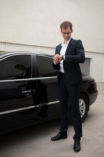 Uomo elegante in piedi accanto alla sua auto per i servizi di taxi