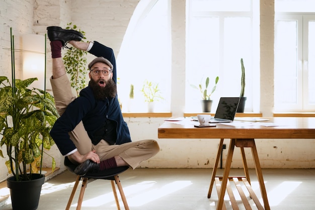 Uomo emotivo che allunga la gamba in ufficio mentre si lavora sul laptop Uomo d'affari a riposo