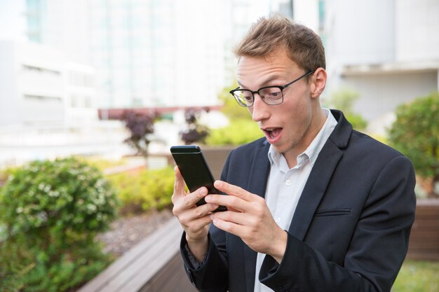 Uomo emozionante con il cellulare che ottiene le notizie scioccanti