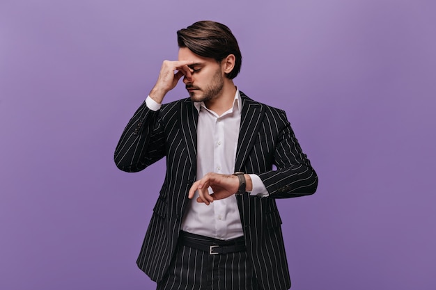 Uomo esausto impegnato con i capelli scuri, camicia chiara e abito a righe che pensa a qualcosa dopo aver guardato l'orologio