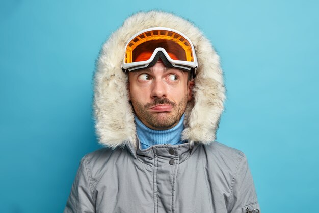 uomo escursionista guarda pensieroso da parte indossa occhiali da sci e giacca invernale con cappuccio ha riposo attivo durante le vacanze gode di sport preferito.
