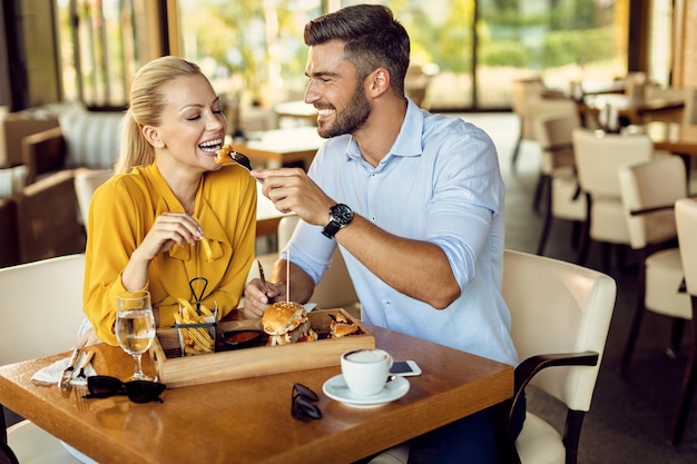 Uomo felice che alimenta la sua ragazza durante il pranzo in un ristorante