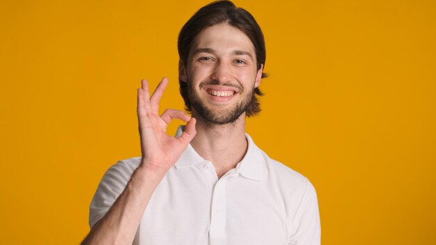 Uomo felice che mostra il segno di approvazione del gesto giusto che dà una risposta positiva su sfondo arancione Ragazzo attraente che afferma che tutto è ok su sfondo colorato