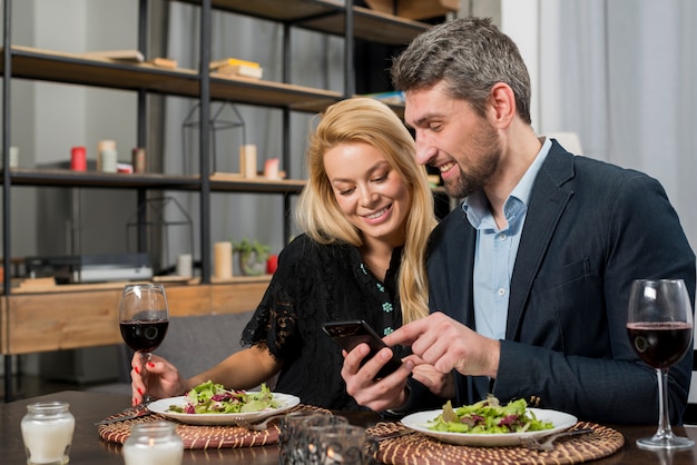 Uomo felice che punta su smartphone per donna allegra al tavolo