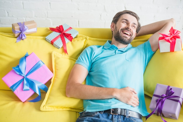 Uomo felice che si distende sul divano circondato da vari regali di compleanno