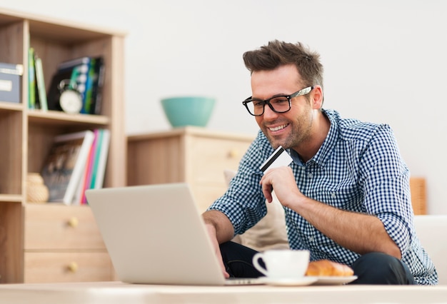 Uomo felice che si siede sul divano con laptop e carta di credito