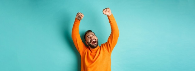 Uomo felice che trionfa e si sente gioito per la vittoria che celebra la vittoria in piedi sul bac azzurro