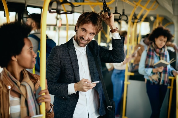 Uomo felice che usa il telefono cellulare e parla con un passeggero mentre si sposta in autobus