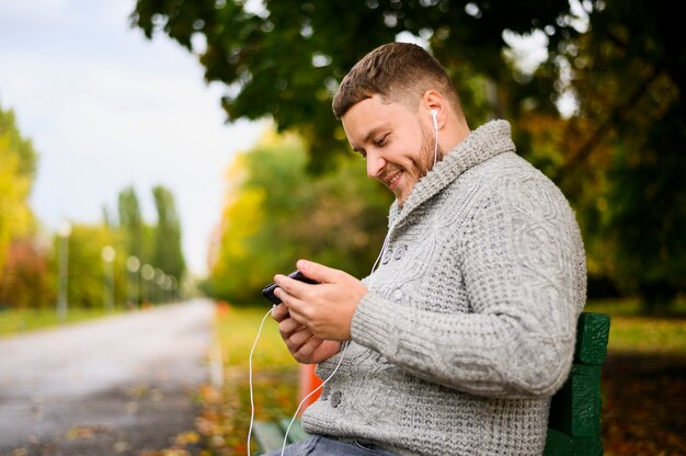 Uomo felice con lo smartphone e le cuffie su un banco