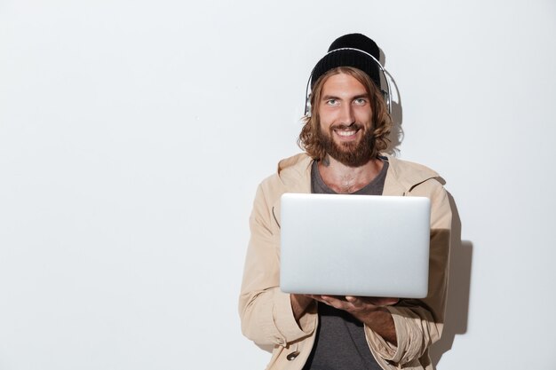 Uomo felice dei pantaloni a vita bassa che usando musica d'ascolto del computer portatile.