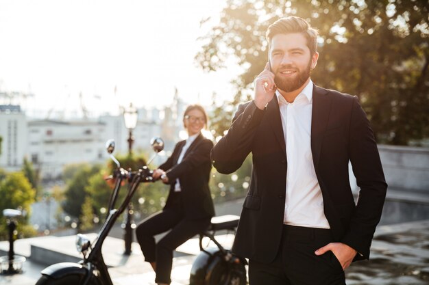 Uomo felice di affari che posa all'aperto che parla dal telefono