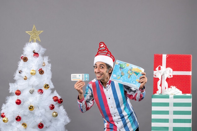 Uomo felice di vista frontale con il cappello di santa della molla a spirale che tiene la mappa del mondo e il biglietto di viaggio