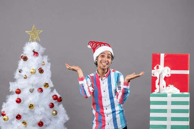 Uomo felice di youg di vista frontale che sta con le mani aperte vicino all'albero di Natale bianco