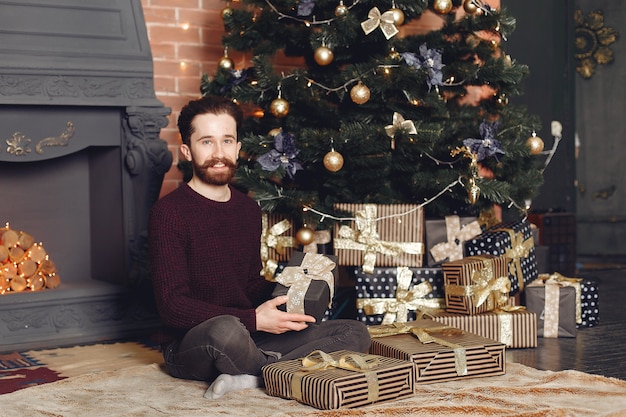 Uomo felice in maglione rosso. Ragazzo davanti al caminetto. Maschio sullo sfondo dell'albero di Natale.