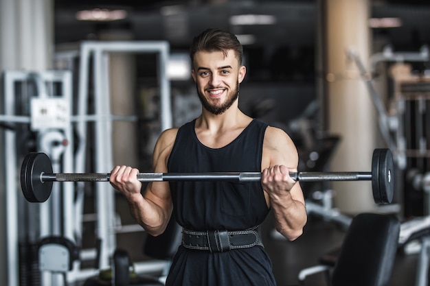 Uomo forte, culturista in abbigliamento sportivo con manubri in palestra, che si esercita con un bilanciere