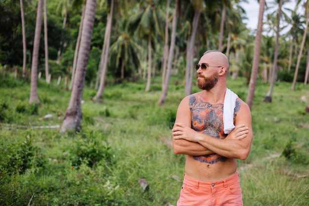 Uomo forte tatuato sul campo tropicale della giungla senza camicia