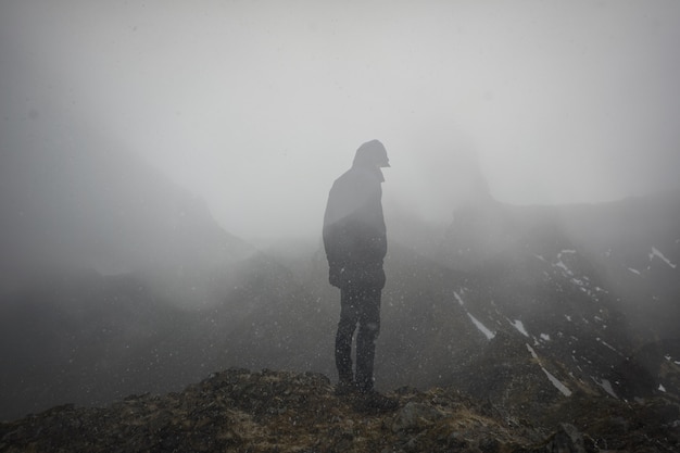 uomo freddo in piedi sul bordo di una montagna nebbiosa