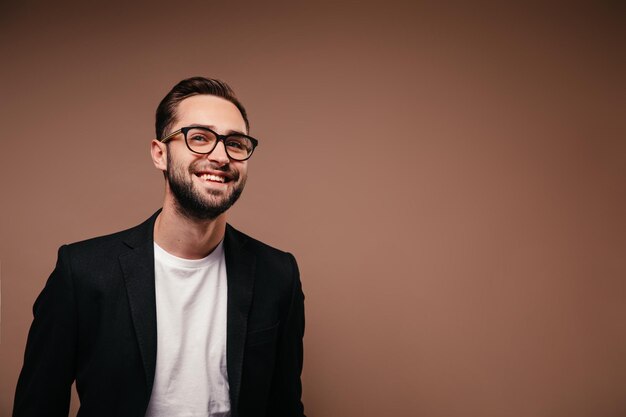 Uomo gioioso in maglietta bianca e giacca sorridente su sfondo marrone