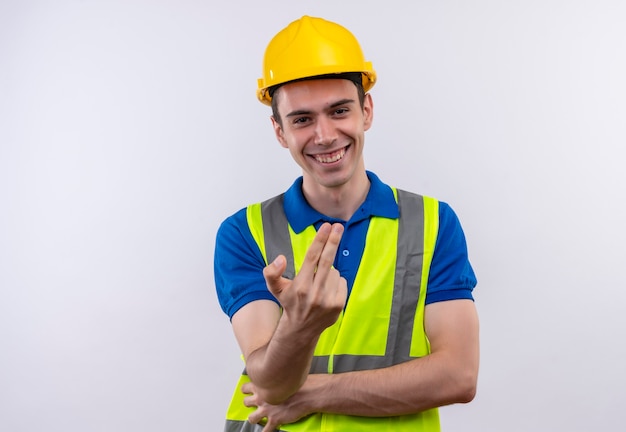 Uomo giovane costruttore indossa uniforme da costruzione e casco di sicurezza sorride e mostra le dita