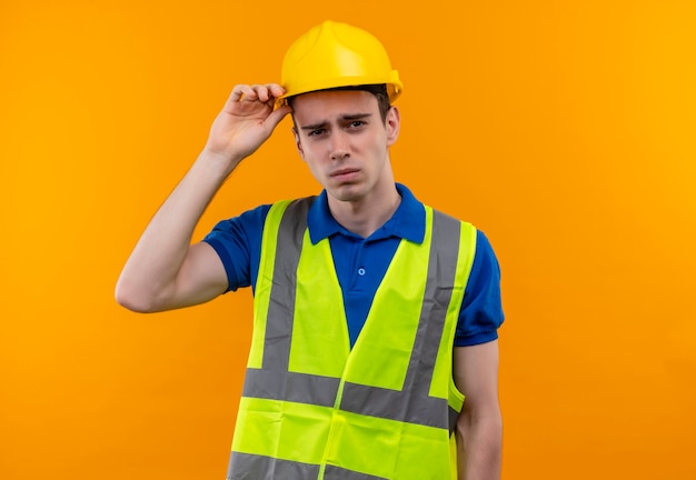 Uomo giovane costruttore indossa uniforme da costruzione e casco di sicurezza