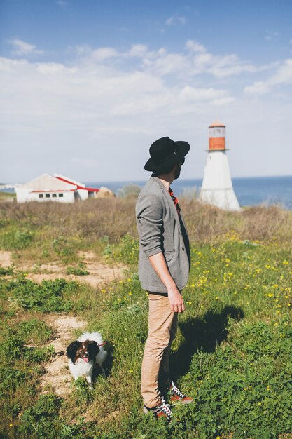 Uomo giovane hipster alla moda in cappello che cammina con il cane in campagna