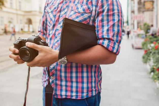 Uomo giovane hipster bello che cammina con la macchina fotografica sulla vecchia strada della città