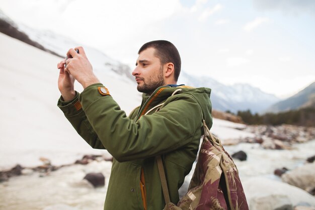 Uomo giovane hipster, scattare foto utilizzando smartphone, natura selvaggia, vacanze invernali, escursionismo