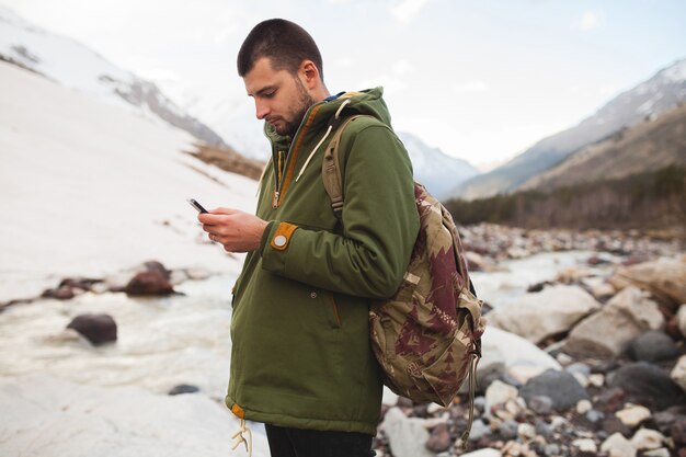 Uomo giovane hipster utilizzando smartphone, natura selvaggia, vacanze invernali, escursionismo