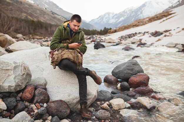 Uomo giovane hipster utilizzando smartphone, natura selvaggia, vacanze invernali, escursionismo