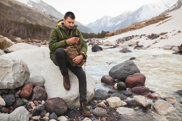 Uomo giovane hipster utilizzando smartphone, natura selvaggia, vacanze invernali, escursionismo