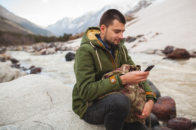 Uomo giovane hipster utilizzando smartphone, natura selvaggia, vacanze invernali, escursionismo