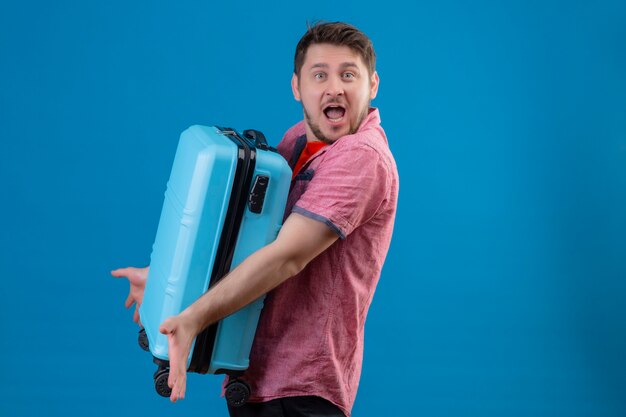 Uomo giovane viaggiatore bello che tiene la valigia blu che sembra confusa