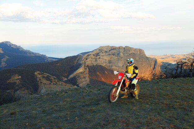 Uomo in attrezzatura sportiva in sella a una moto da cross in montagna