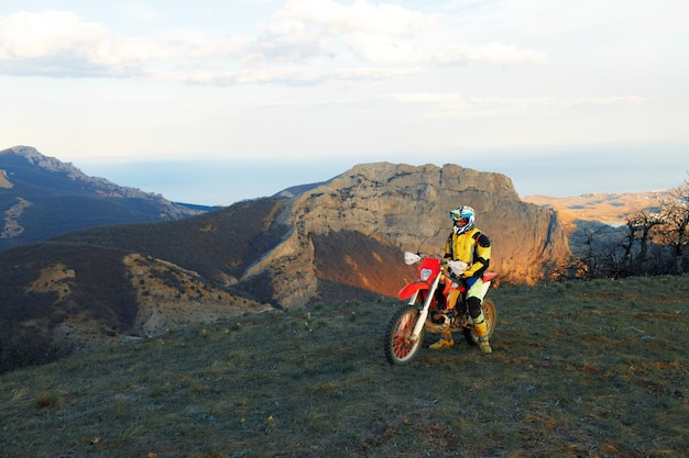 Uomo in attrezzatura sportiva in sella a una moto da cross in montagna