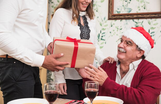 Uomo in bianco dando scatola regalo al vecchio uomo in cappello di Babbo Natale