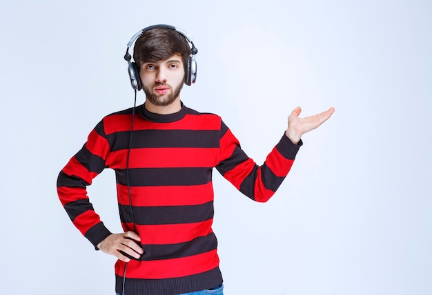 Uomo in camicia a righe rossa che indossa le cuffie e indica il lato destro.