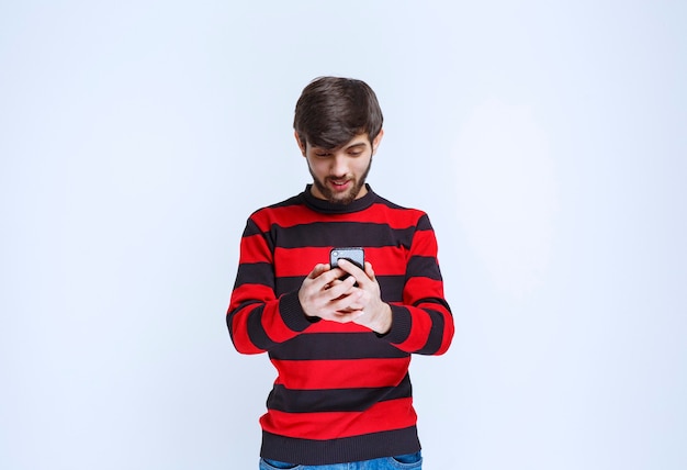 Uomo in camicia a righe rosse che chiacchiera o manda un sms al suo smartphone.