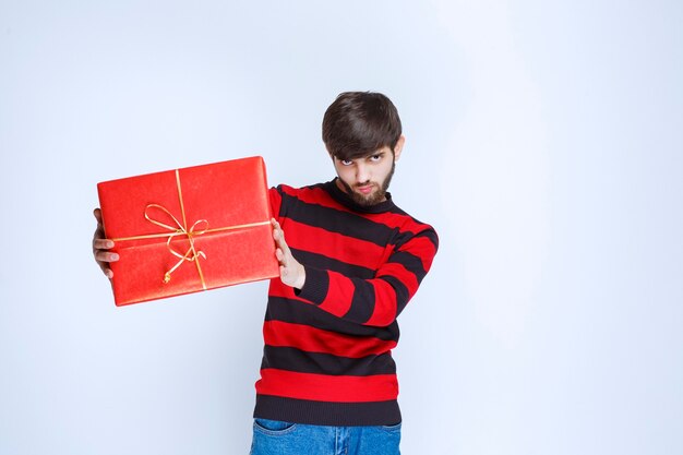 Uomo in camicia a righe rosse che tiene in mano una confezione regalo rossa, che la consegna e la presenta al cliente o alla sua ragazza.