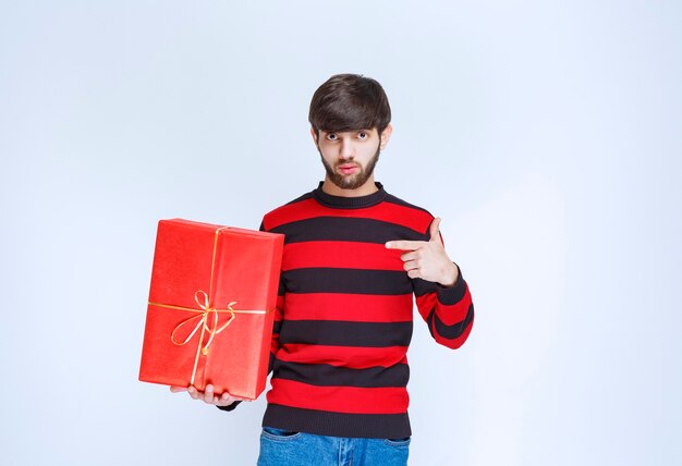 Uomo in camicia a righe rosse che tiene una confezione regalo rossa e la promuove.