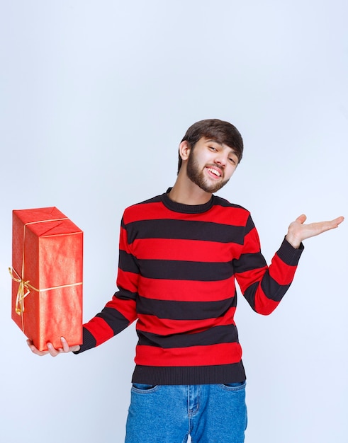 Uomo in camicia a righe rosse che tiene una confezione regalo rossa e la promuove.