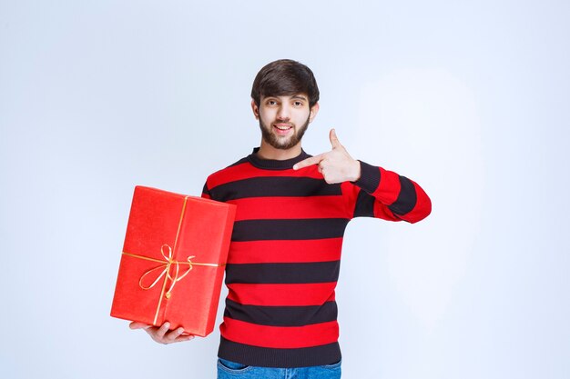 Uomo in camicia a righe rosse che tiene una confezione regalo rossa e la promuove.