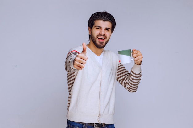 Uomo in camicia bianca che tiene una tazza di caffè e che fa buon segno della mano.