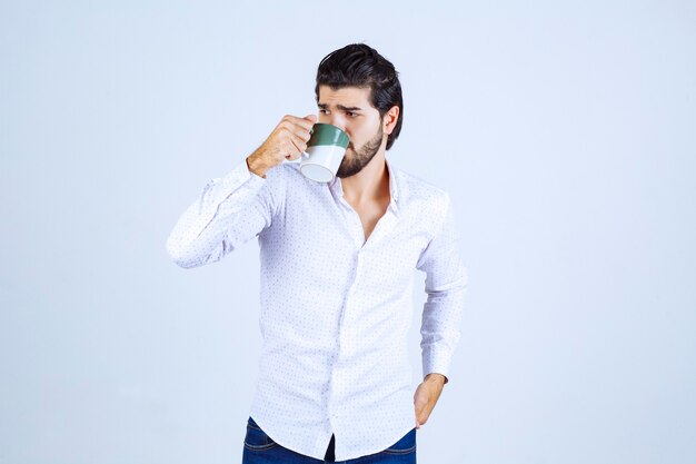 Uomo in camicia bianca che tiene una tazza di caffè e la beve
