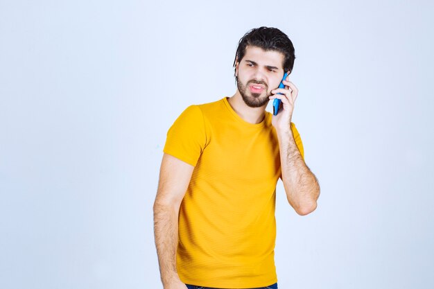 Uomo in camicia gialla che parla al telefono.