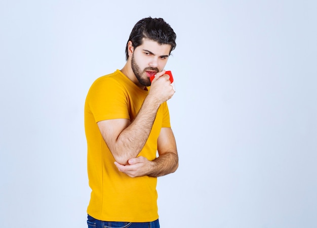 Uomo in camicia gialla che tiene una tazza di caffè e sembra misterioso.