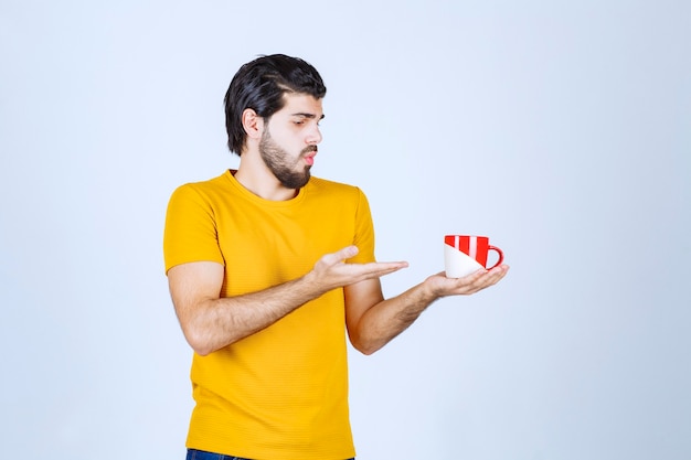 Uomo in camicia gialla che tiene una tazza rossa e pensa.