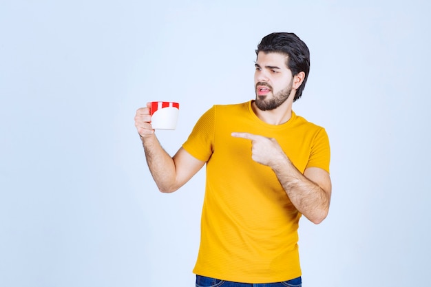 Uomo in camicia gialla che tiene una tazza rossa e pensa.