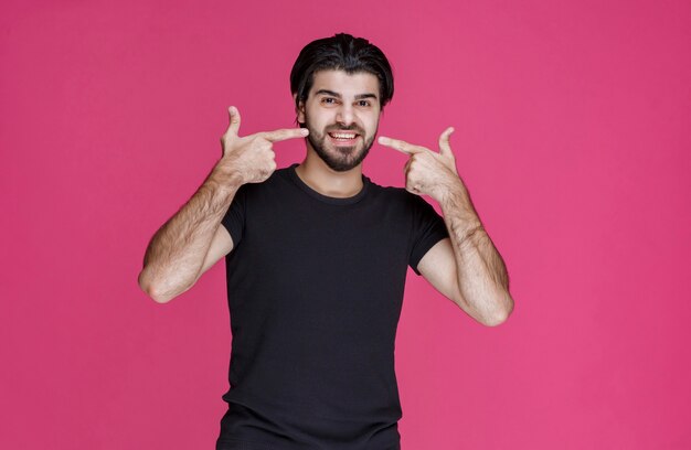 Uomo in camicia nera che punta la bocca e chiede sorridendo