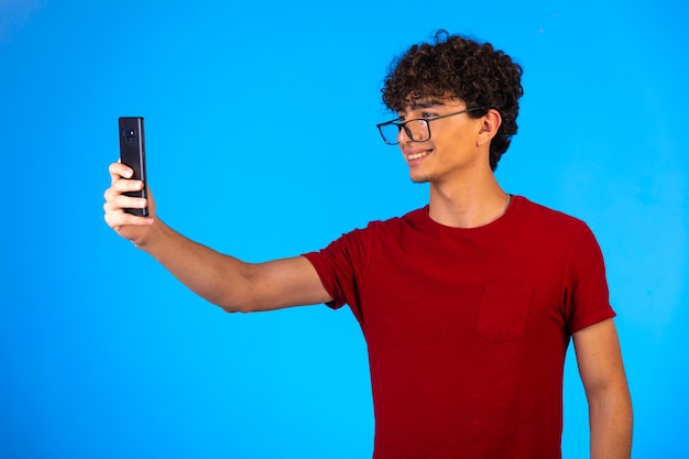 Uomo in camicia rossa prendendo selfie o facendo una telefonata e divertirsi su sfondo blu.