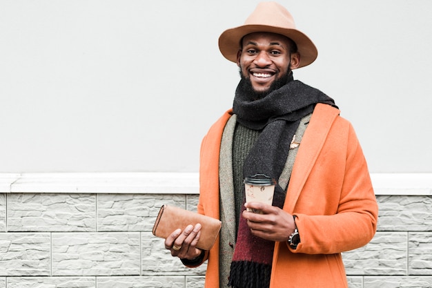 Uomo in cappotto arancione che tiene una tazza di caffè e il suo portafoglio